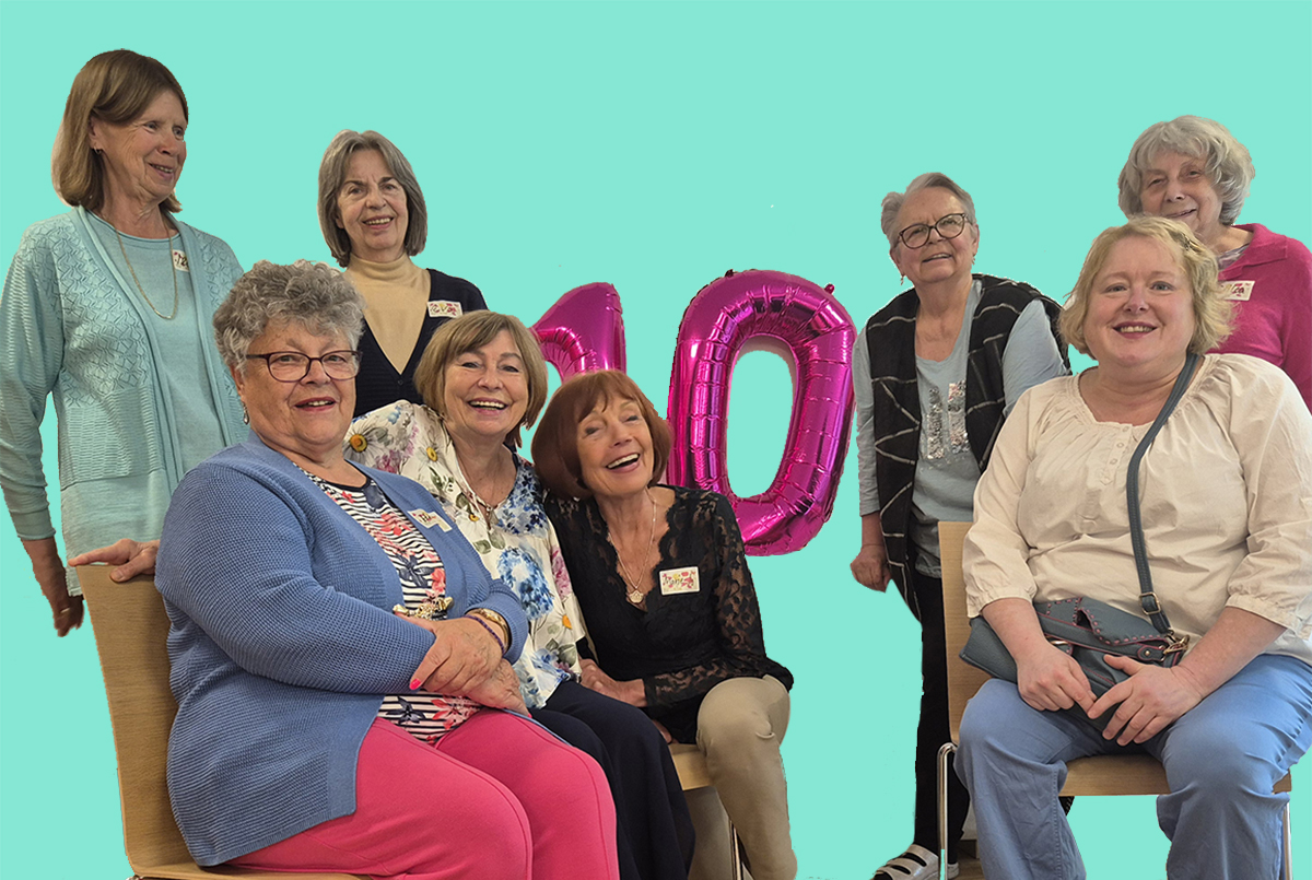 die 8 Frauen von WG 3 lachen fröhlich in die Kamera vor türkisem Hintergrund